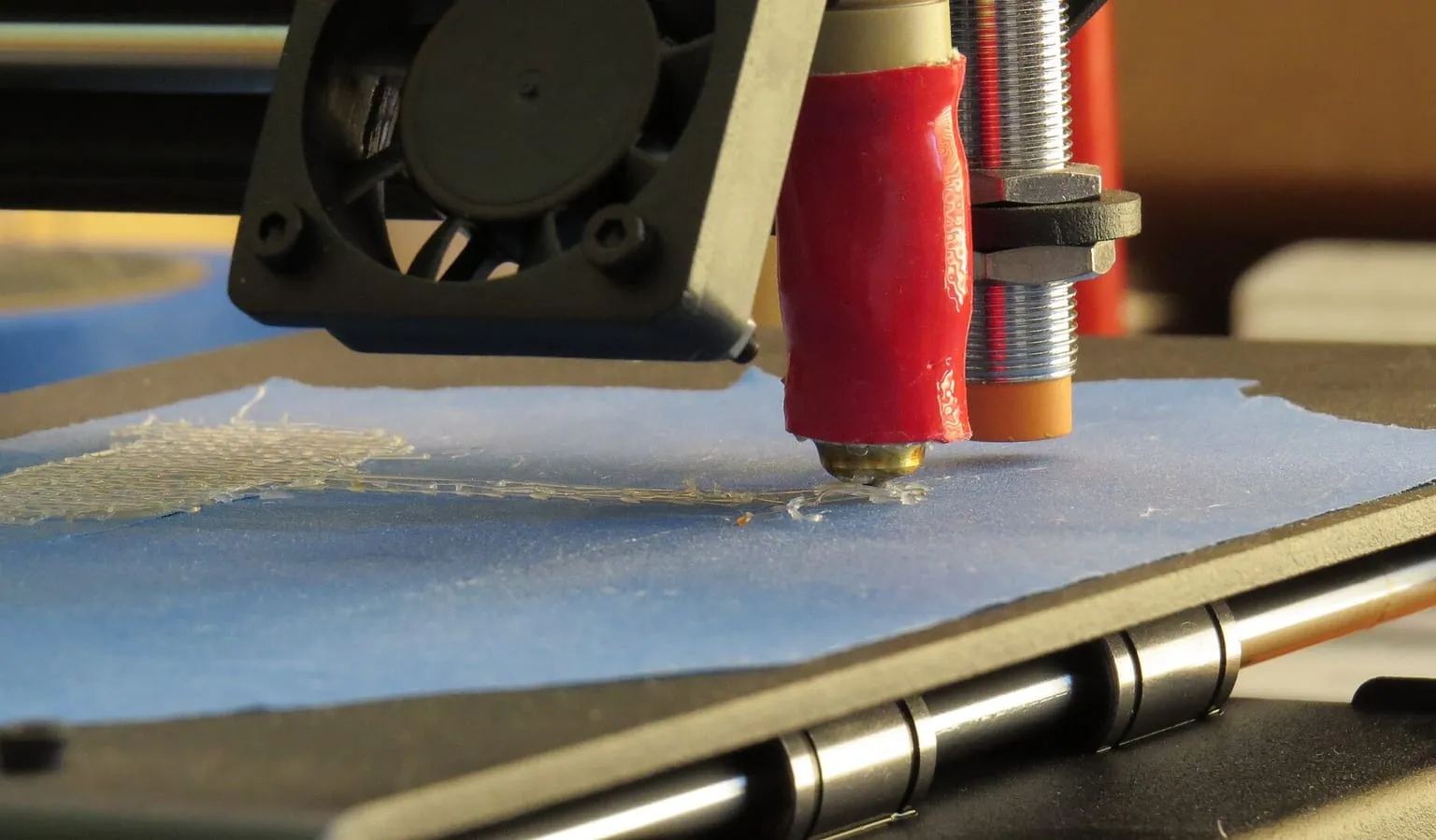 A nozzle laying down the first layer on blue tape, with an inductive probe beside it